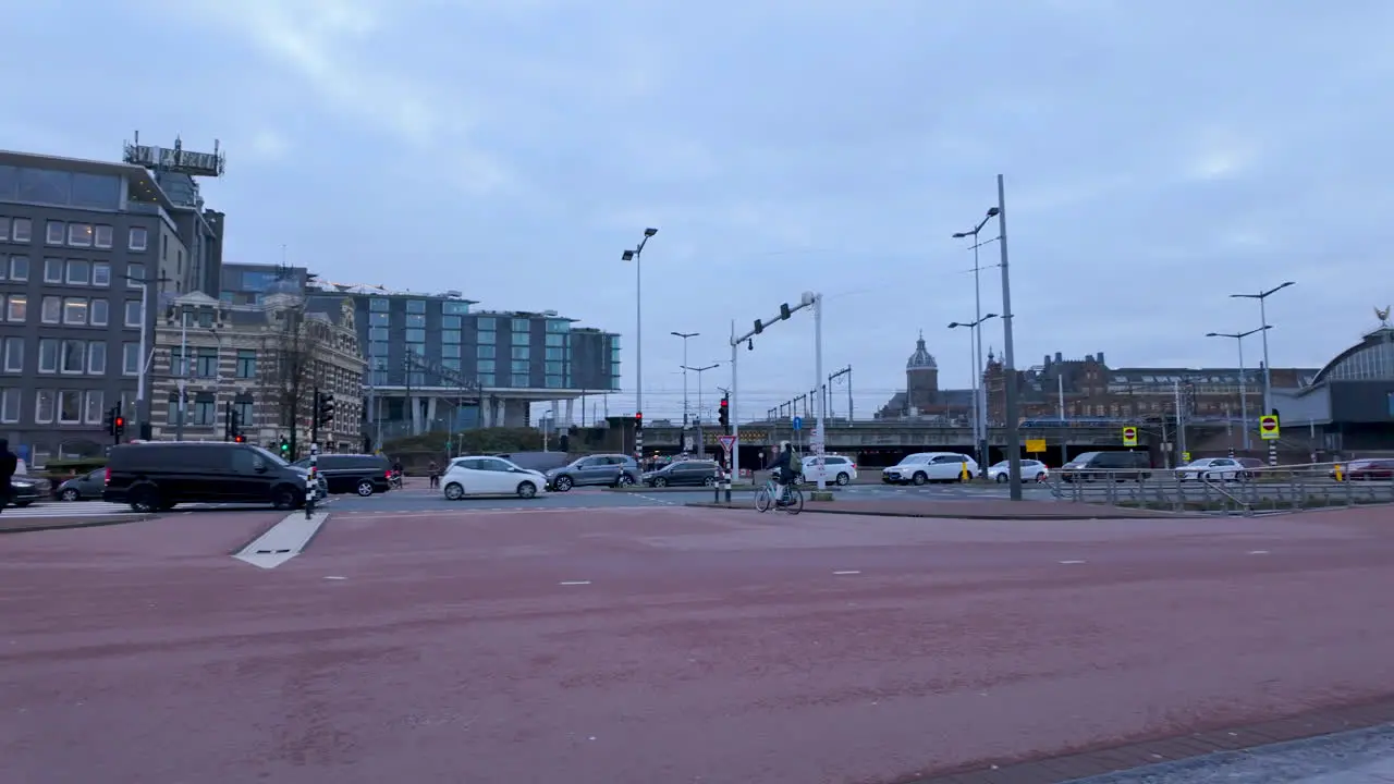 A wide street with multiple lanes for cars and bikes and a tram or train station in the background