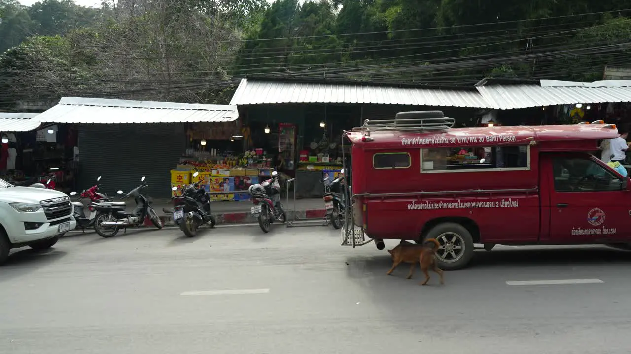 Red van driving past local shops and motorbikes on a busy street in the city of Chiang Mai Thailand