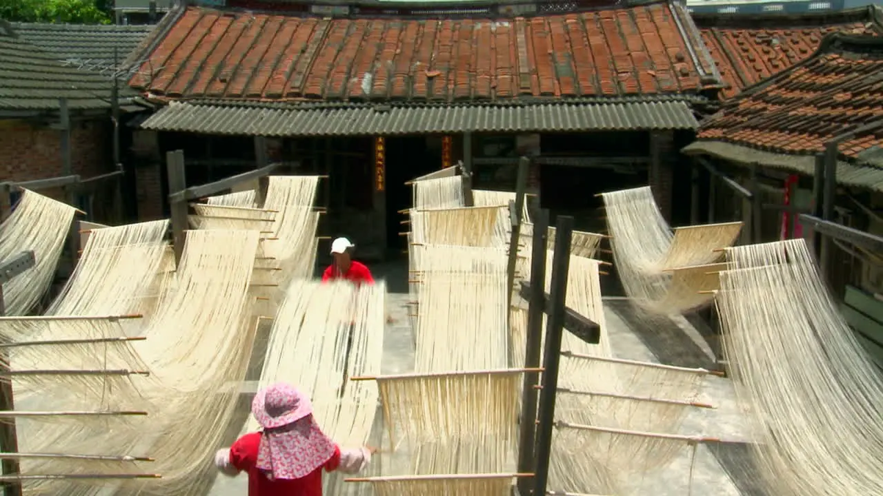 Workers carry strands of soft fresh noodles into courtyard on long poles shake noodles then hang in racks to dry in sunlight