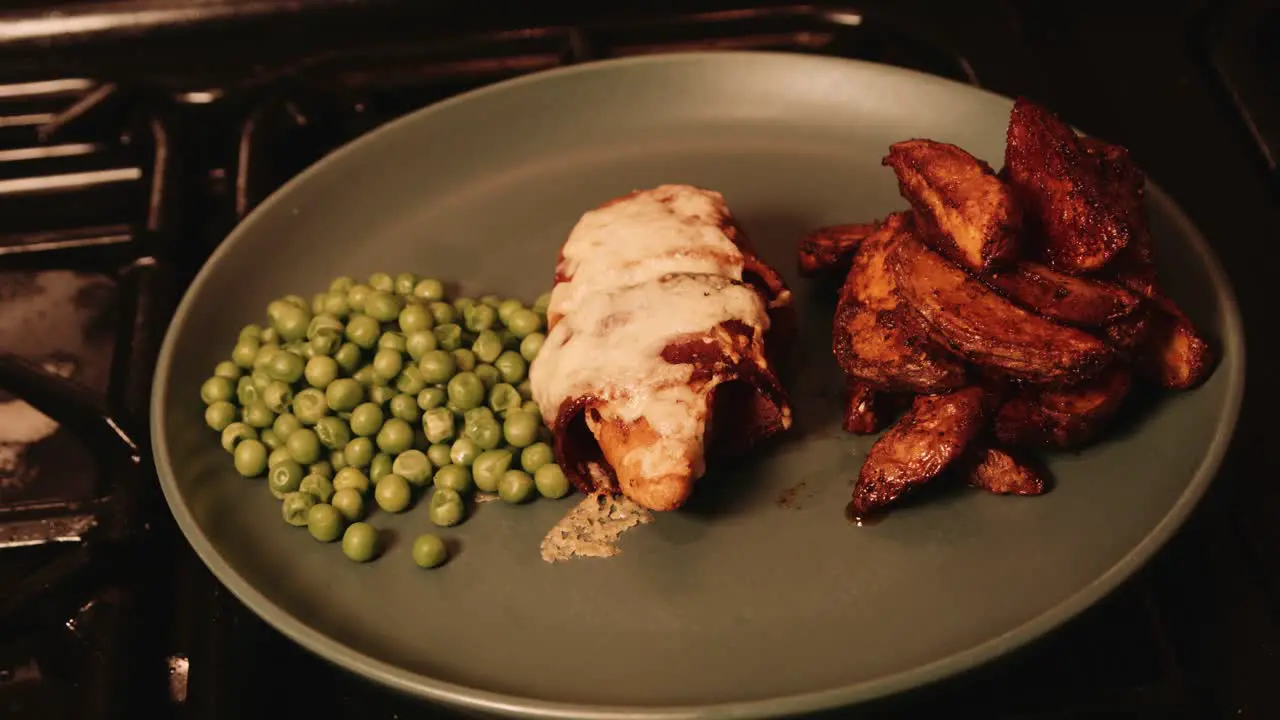 Plated PlantBased Chicken Fillet Wrapped in Vegan Bacon with Paprika Potato Wedges and Peas