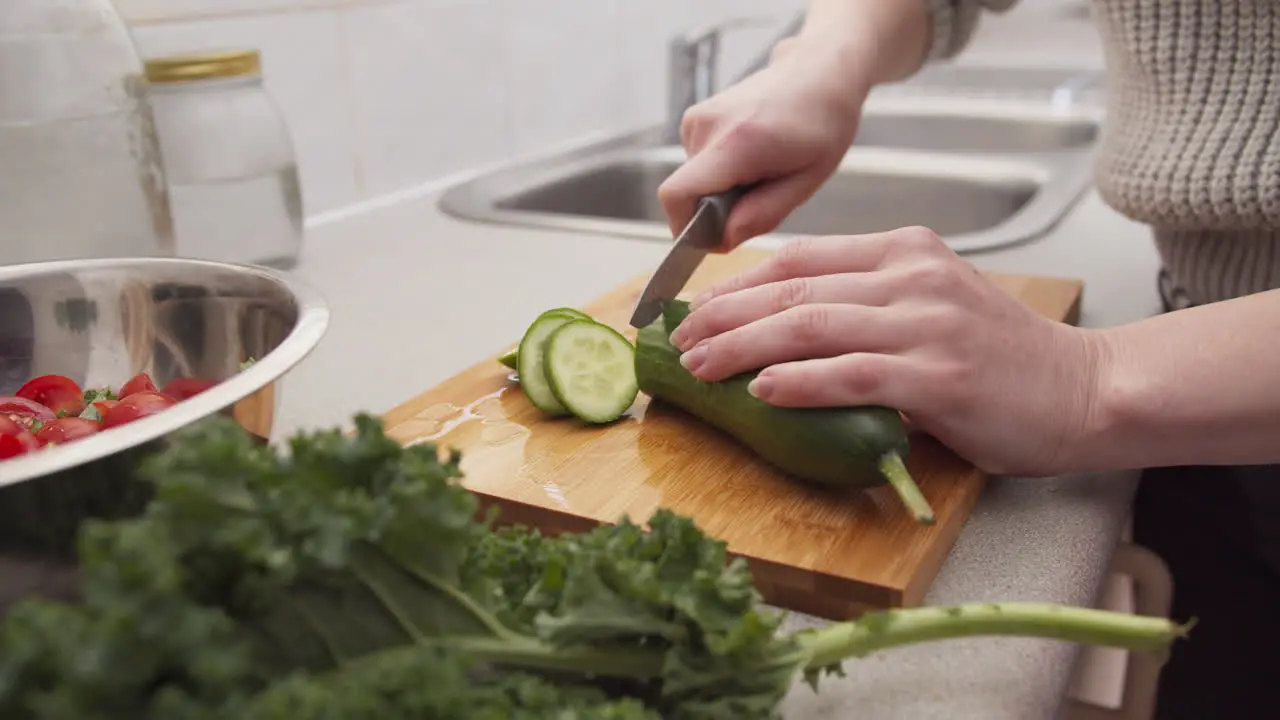 Hands cutting cucumber for a salad with greens on the foreground