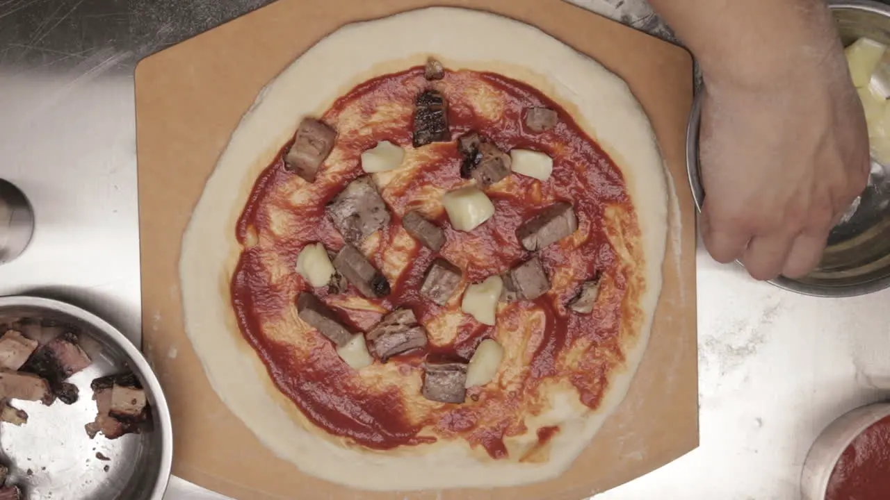 Placing Cubed Cheese On Pizza Dough Topped With Meat And Pizza Sauce Before Baking