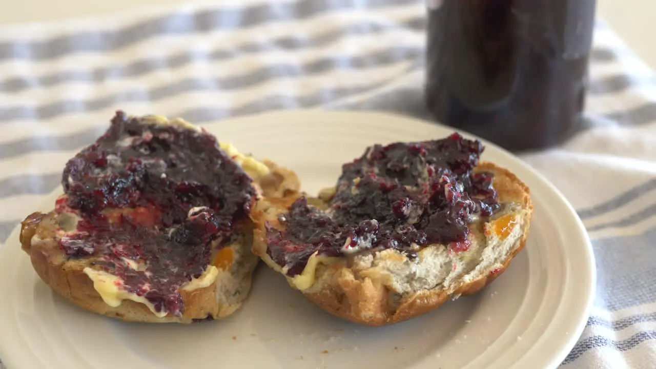 Slow motion pan across hot cross buns sitting on plate with thick butter and jam during Easter