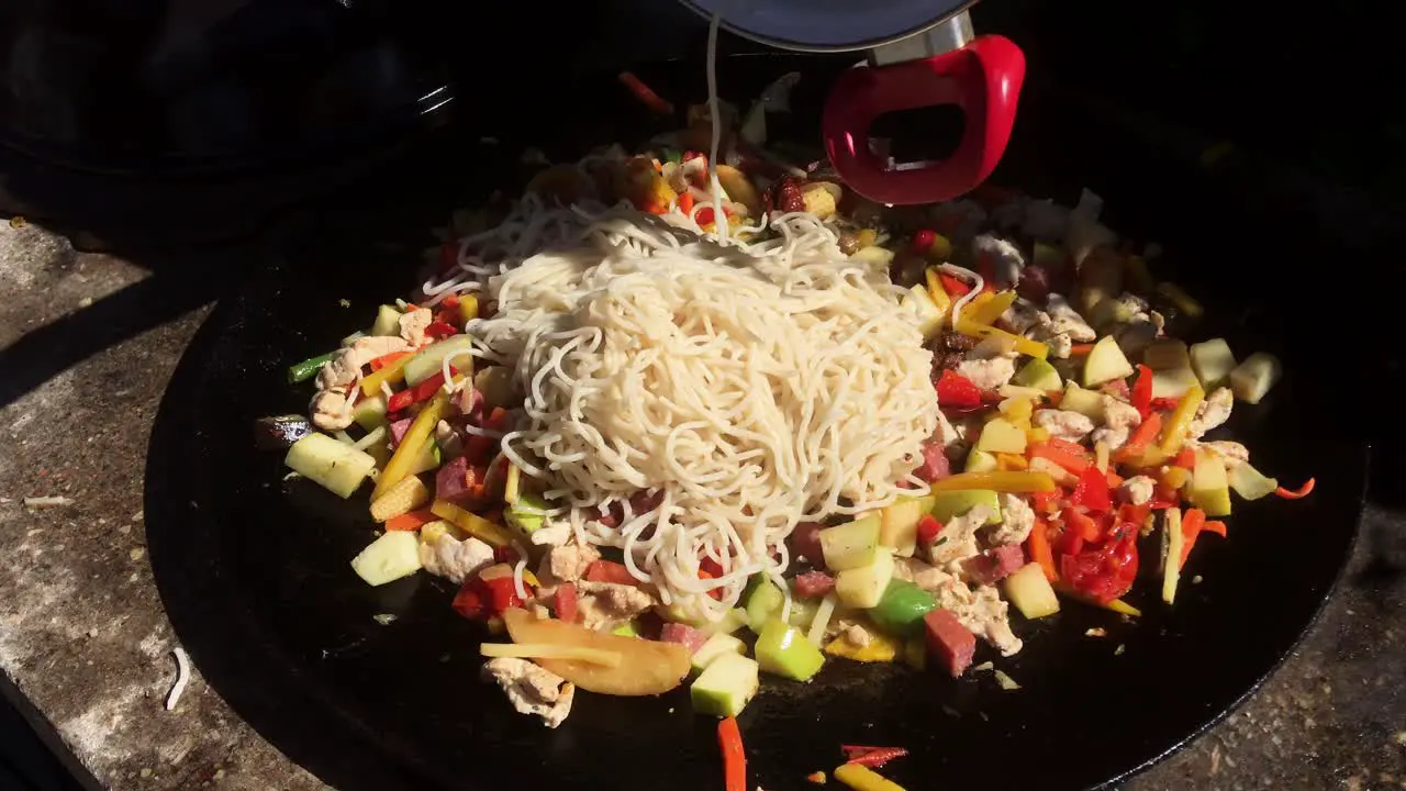 wok cooked outside in large pan noodles being added