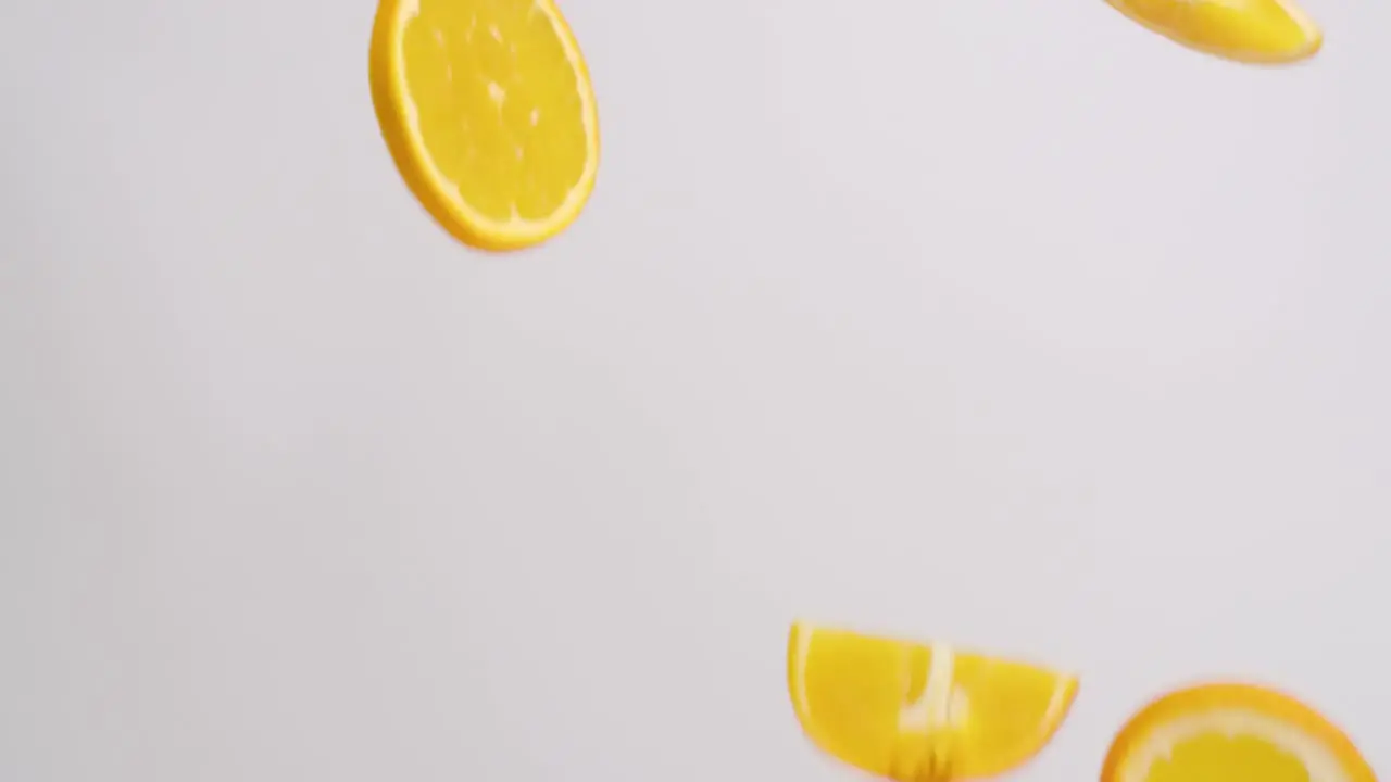 Bright orange citrus orange slices raining on white backdrop in slow motion