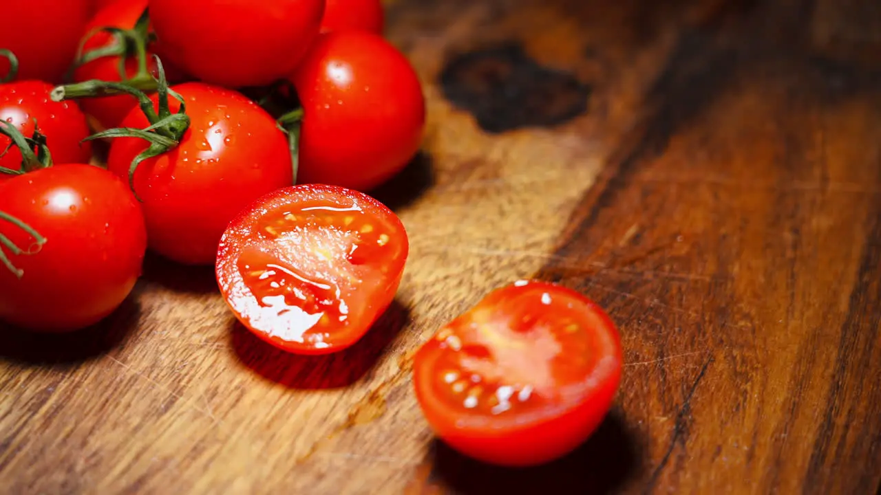 Handheld shot of a male hand cutting a red tomato in half on a wooden cutting board