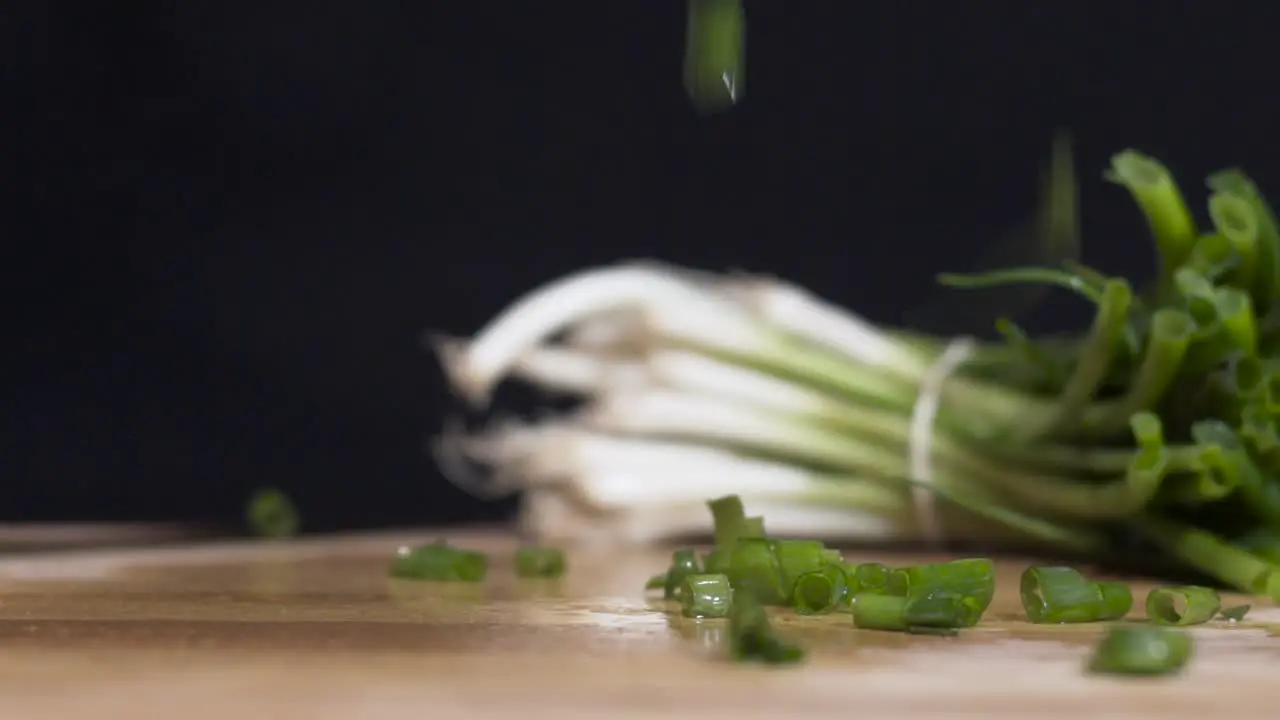 Slow motion close up shot of chopped spring onions-scallions falling with full one in the background