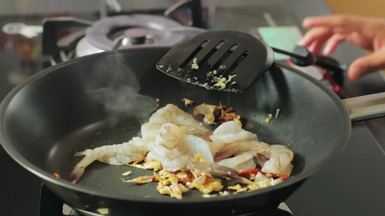 A girl is adding raw peeled shrimps to a hot pan with frying chili and garlic homemade cooking in the kitchen