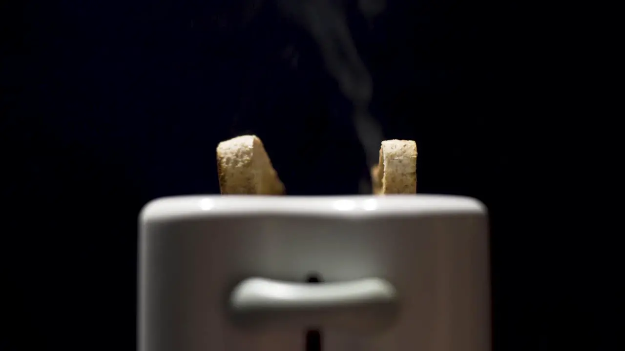 Close up shot of toast steaming and popping up out the toaster with black background