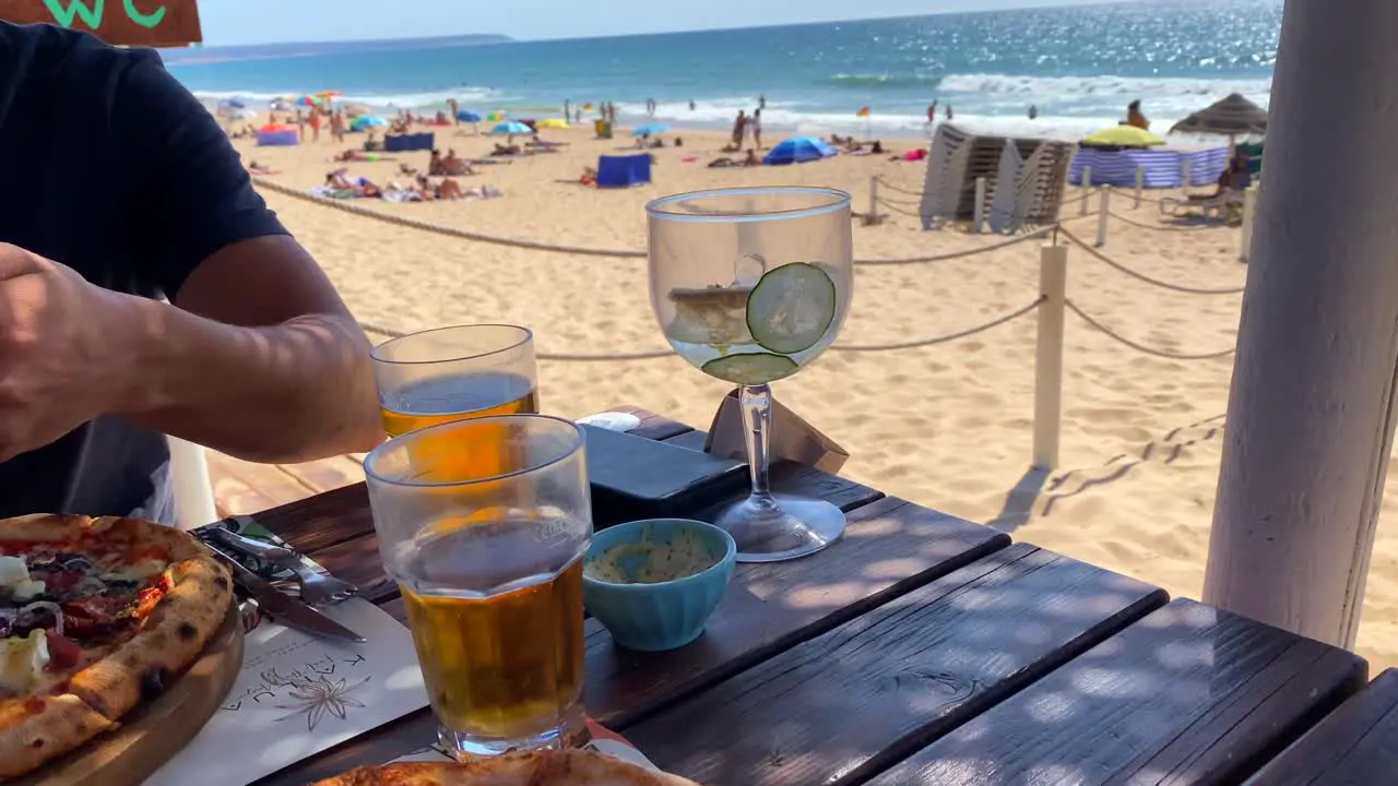 Enjoying two pizzas and drinks at the beach with a beautiful sea view in Lisbon Portugal restaurant in summer on a sunny day with blue sky 4K shot