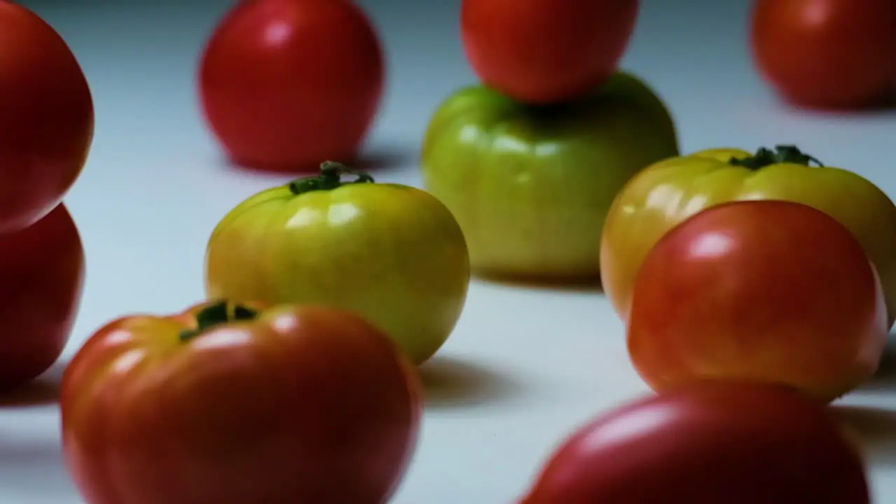 Slow Motion Shot of Big Tomatoes Falling on Other Tomatoes Laying on a White Surface