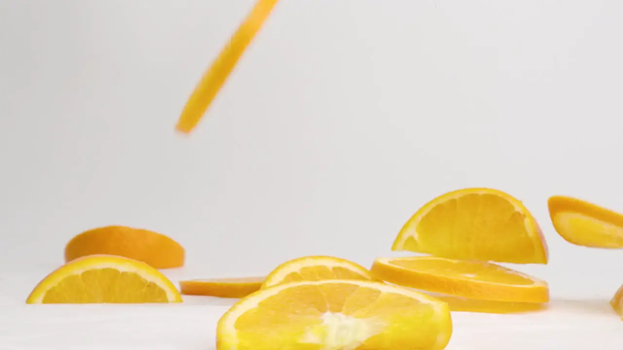 Bright orange citrus slices bouncing on white table top in slow motion