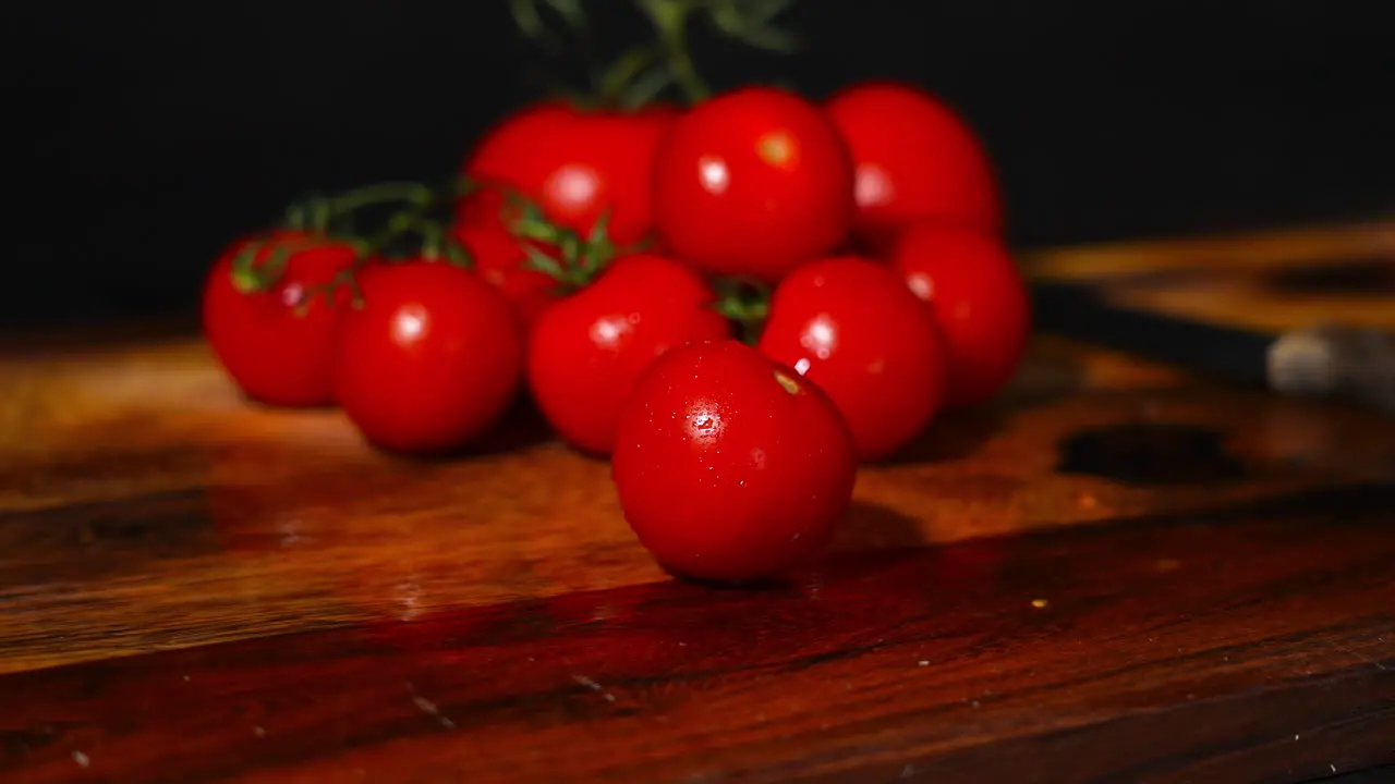 Handheld shot of a tomato falling on a wooden cutting board with a stack of tomatoes in the background