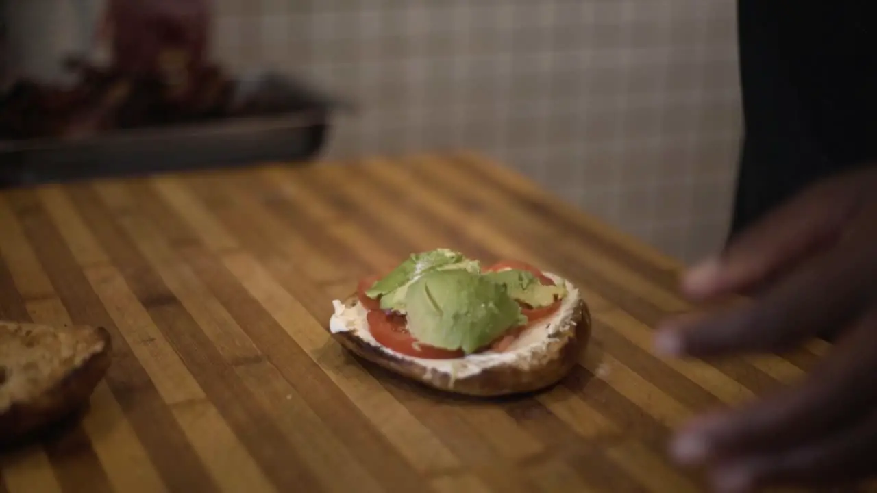 Lady adding salt and bacon to bagel