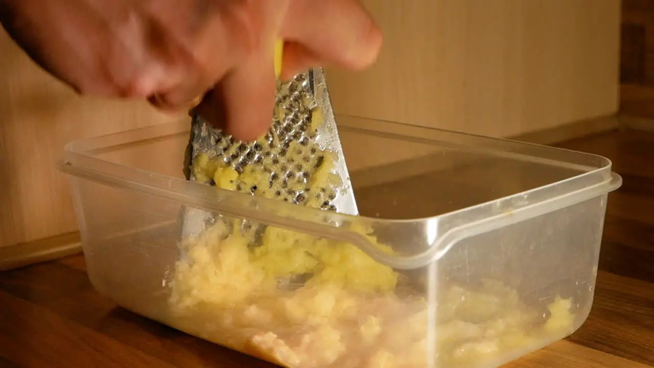 Peeled raw potatoes being grated by a married man in homemade kitche