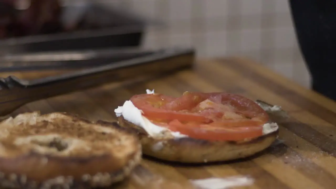 Slow motion close up shot of salt being thrown onto tomato on bagel