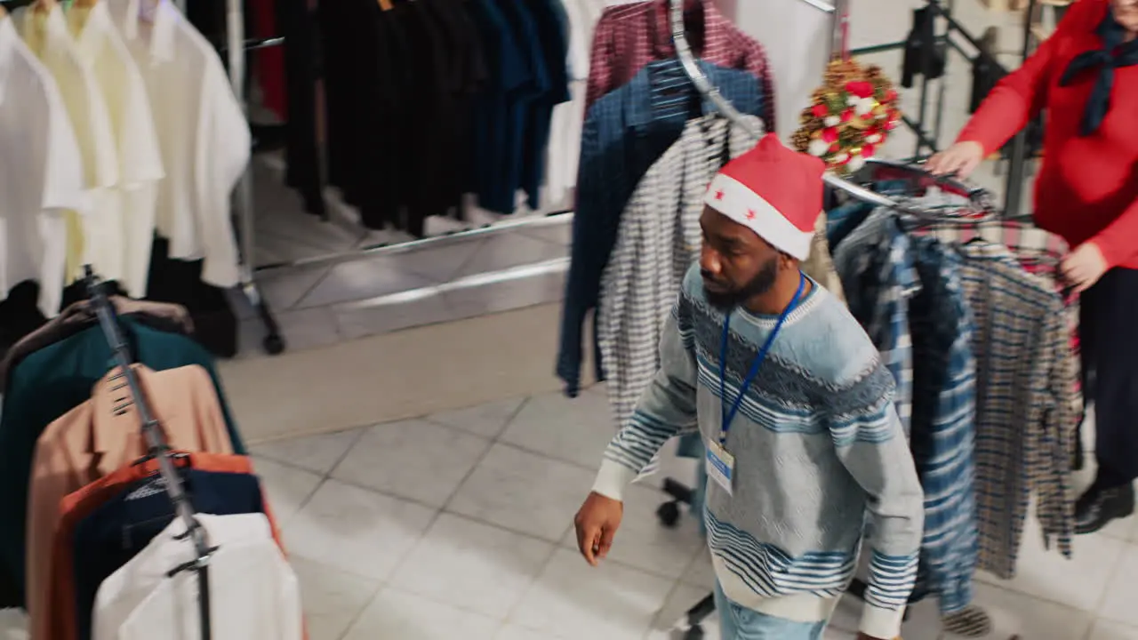 Employees wearing Santa hats and customers walking through Christmas decorated clothing store during festive holiday season Workers and clients in xmas adorn fashion shop