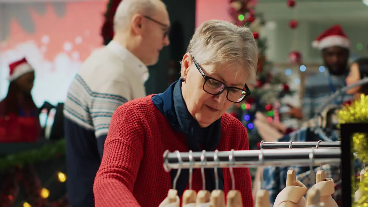 Portrait of elderly woman browsing through clothes in Christmas decorated clothing store during winter holiday season Aged customer at the mall in shopping spree session