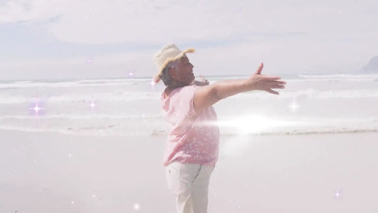 Animation of light spots over happy senior african american woman dancing on sunny beach