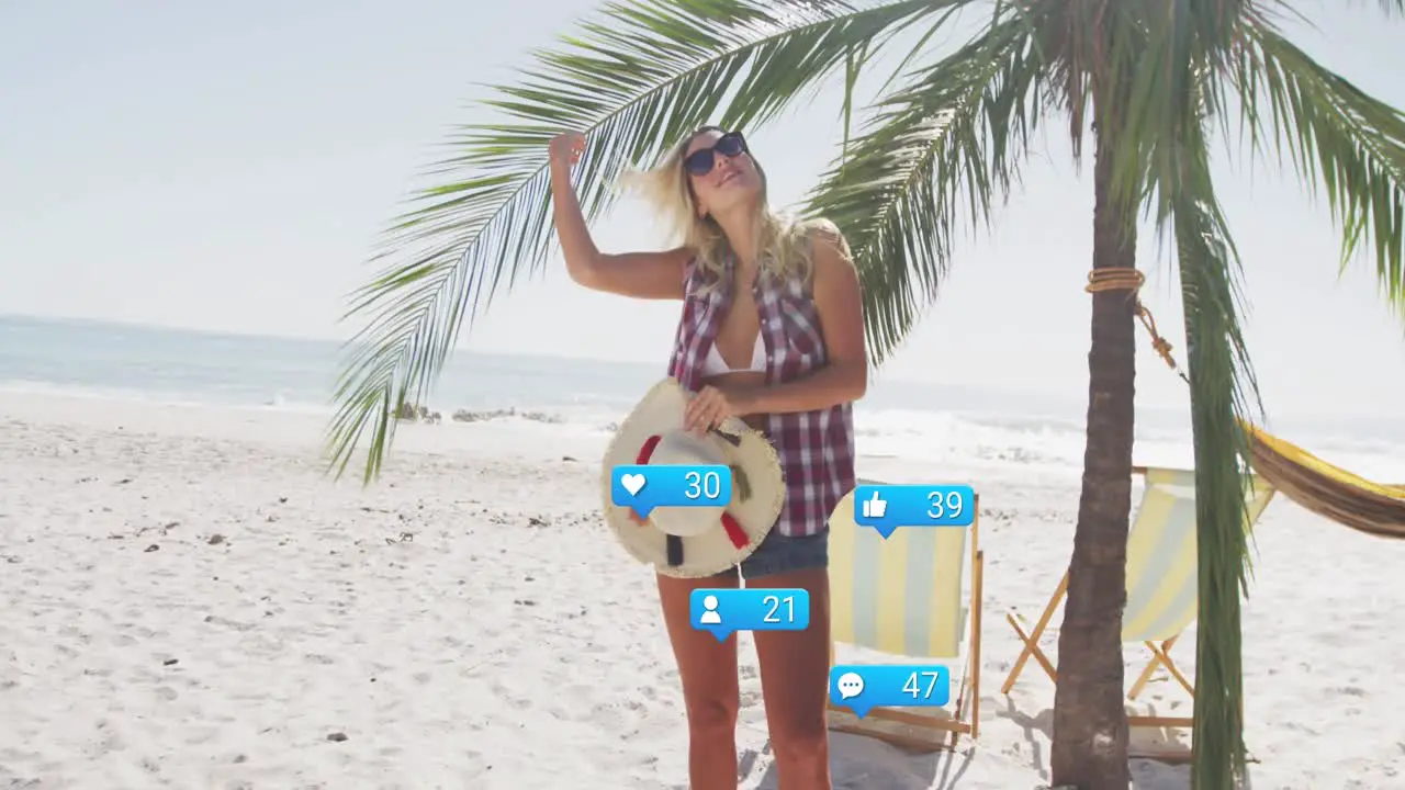 Animation of social media reactions over happy caucasian woman standing under palm on beach