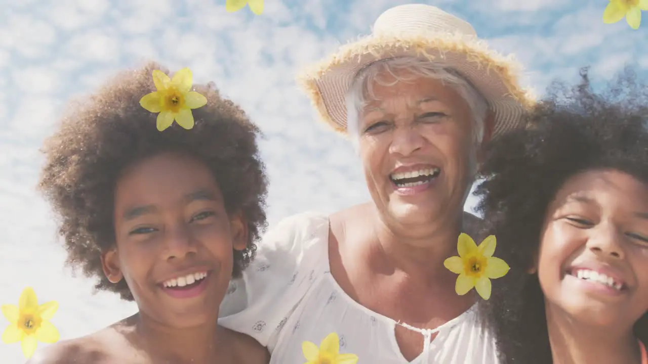 Animation of flowers over happy senior african american woman with grandchildren on sunny beach