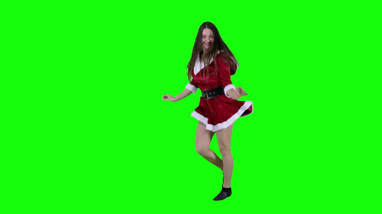 Happy excited female teenager wearing Santa dress having fun at holiday time young woman dance in front of green screen to New Year songs celebrating Xmas alone