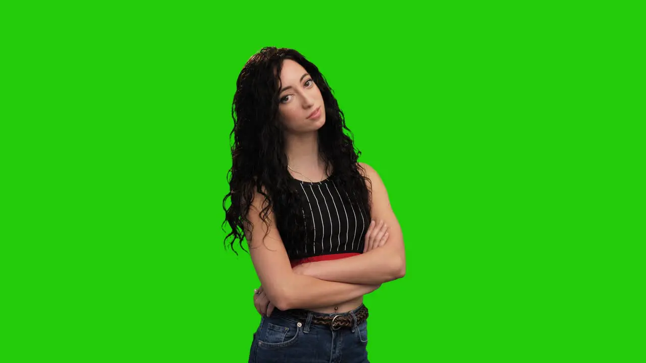 Confident woman with long curly hair crosses hands posing on green screen