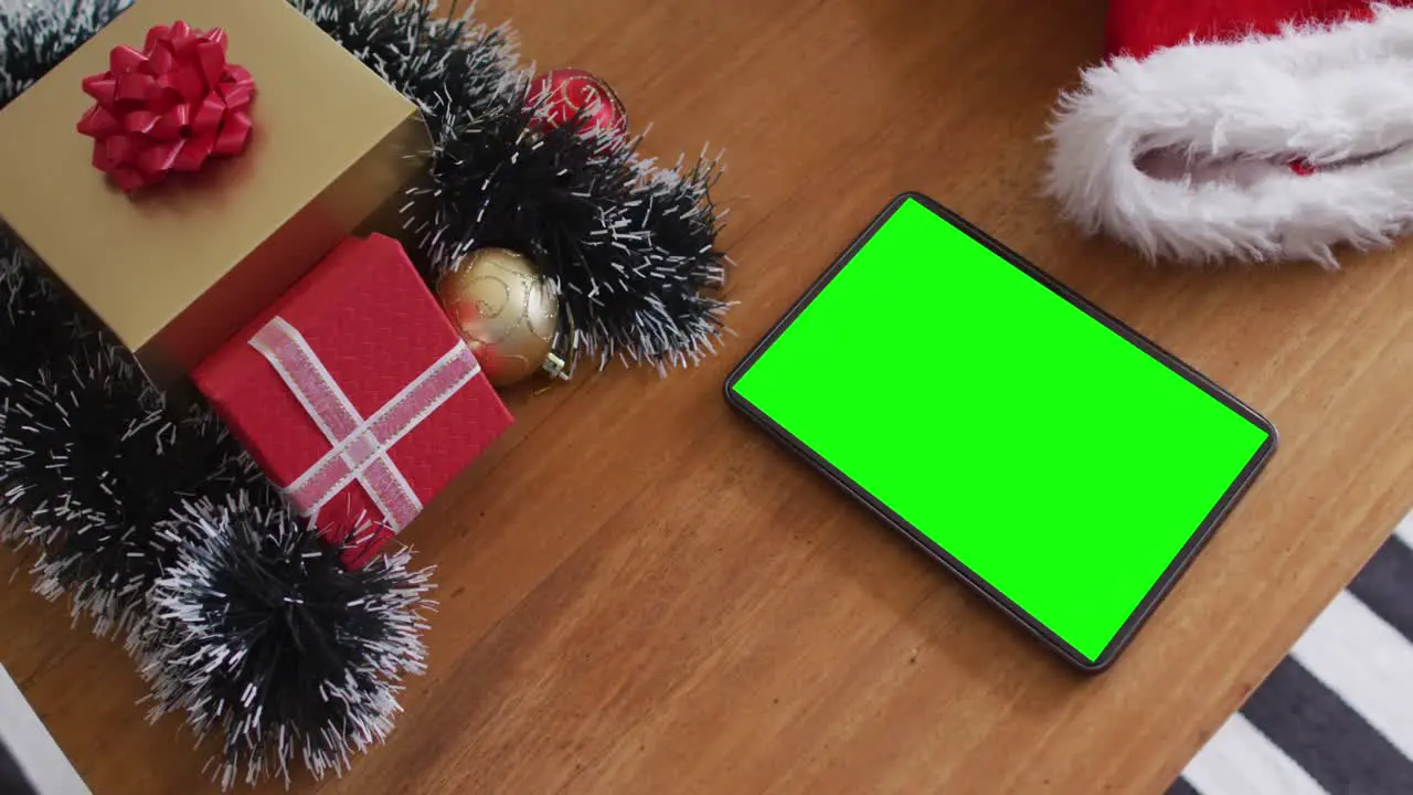 Tablet with green screen on table with santa hats and christmas presents