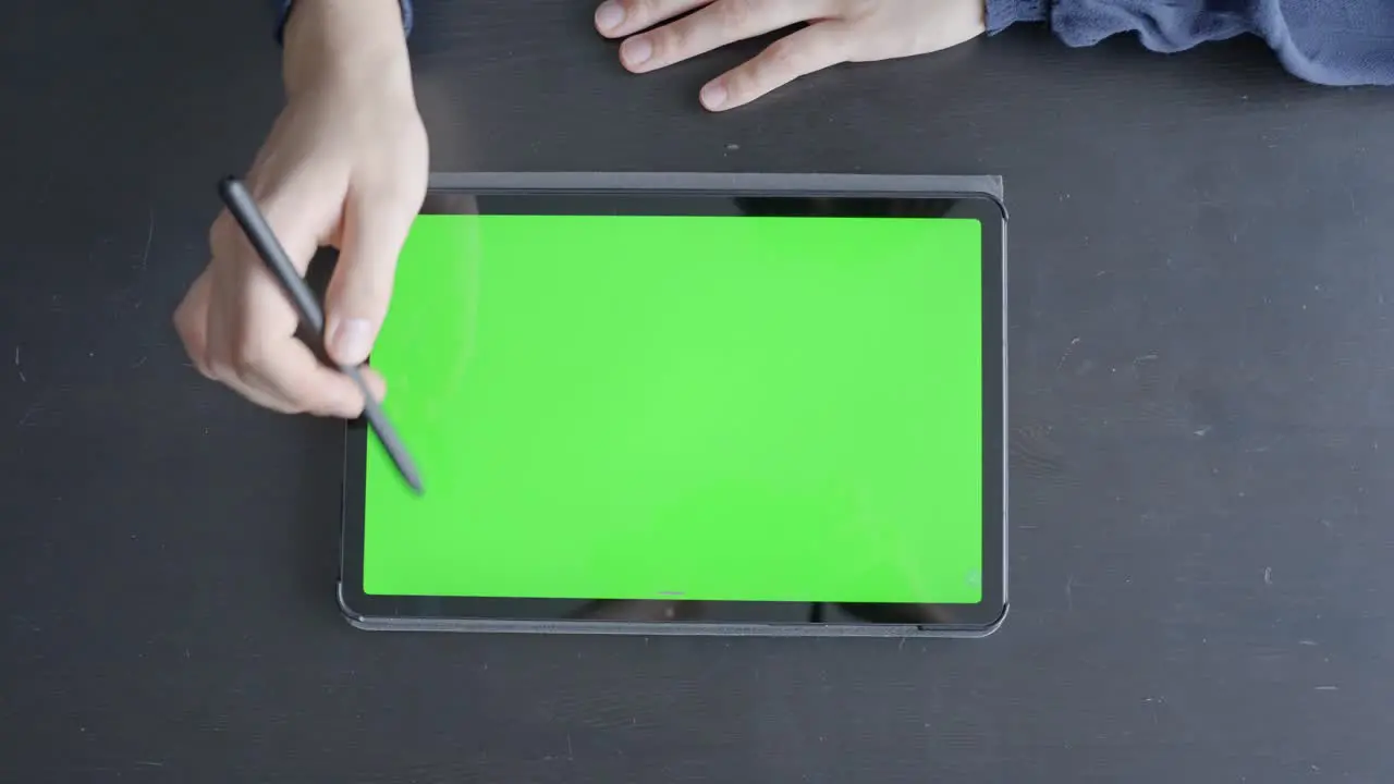 Green screen tablet lays flat on black desk female hands indicating