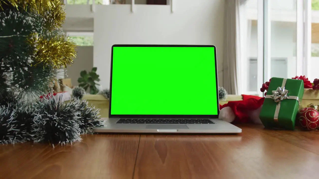 Laptop with green screen copy space on table with santa hats christmas tree and presents