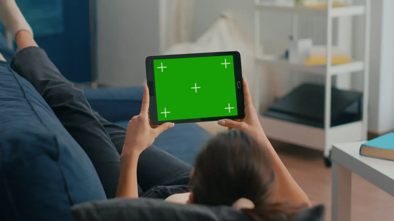 Woman sitting on sofa in living room watching movies on tablet computer