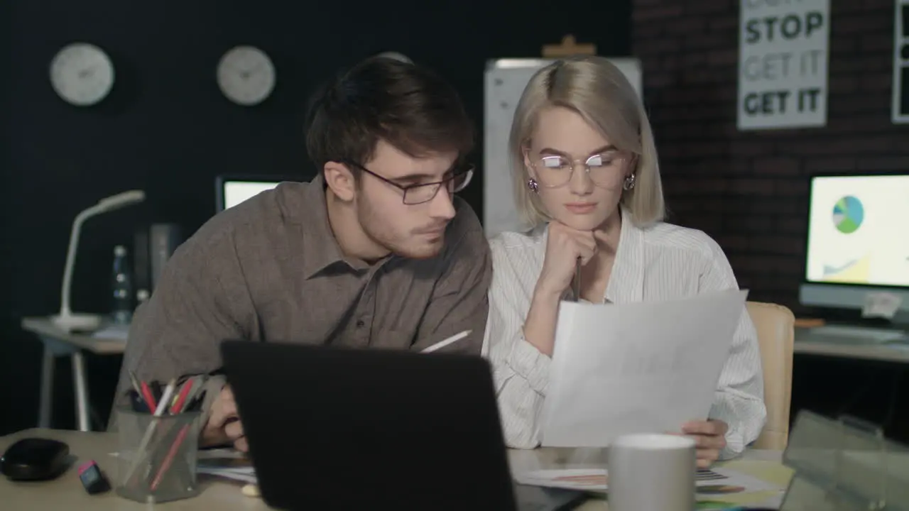 Business couple watching together financial report front computer in dark office