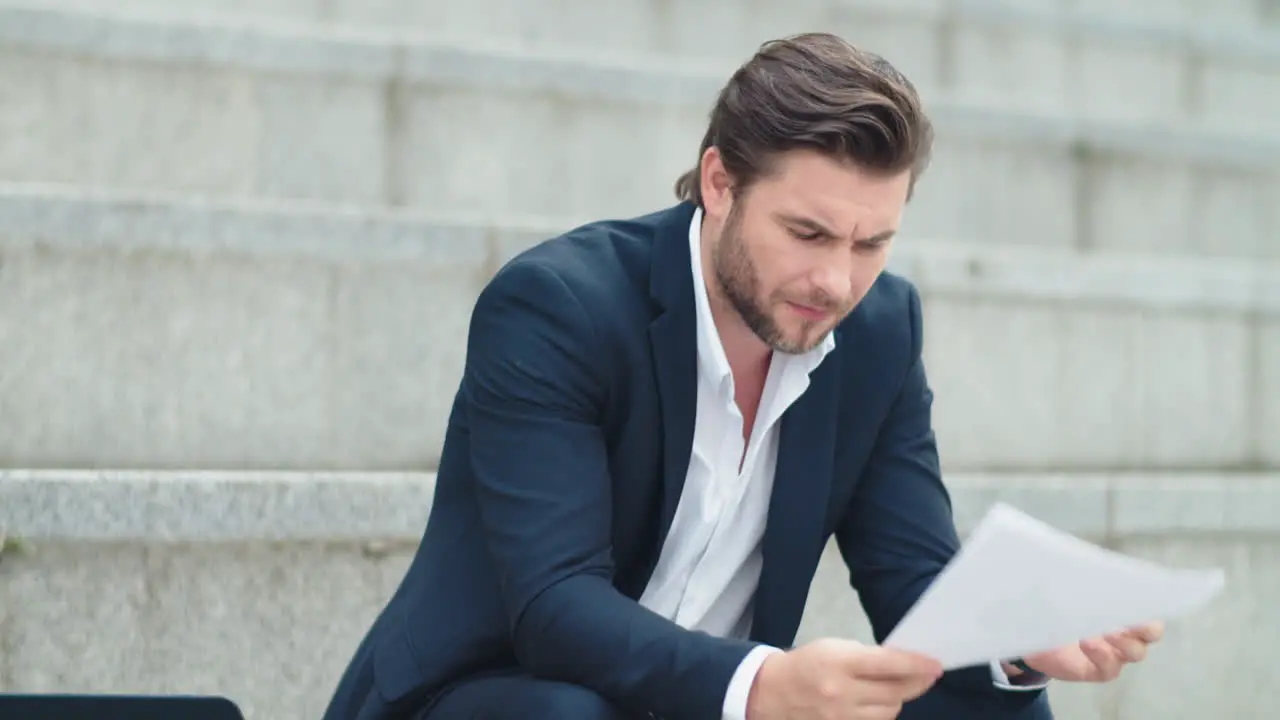 Businessman examining business papers outdoors Male manager sitting on stairs