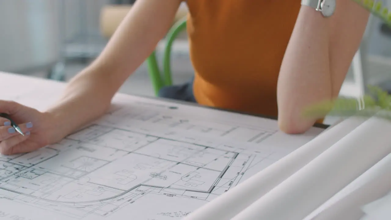 Close Up Of Female Architect In Office Working At Desk Making Notes On Plan Or Blueprint