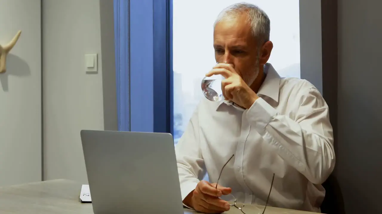 Businessman having a glass of water while using laptop 4k