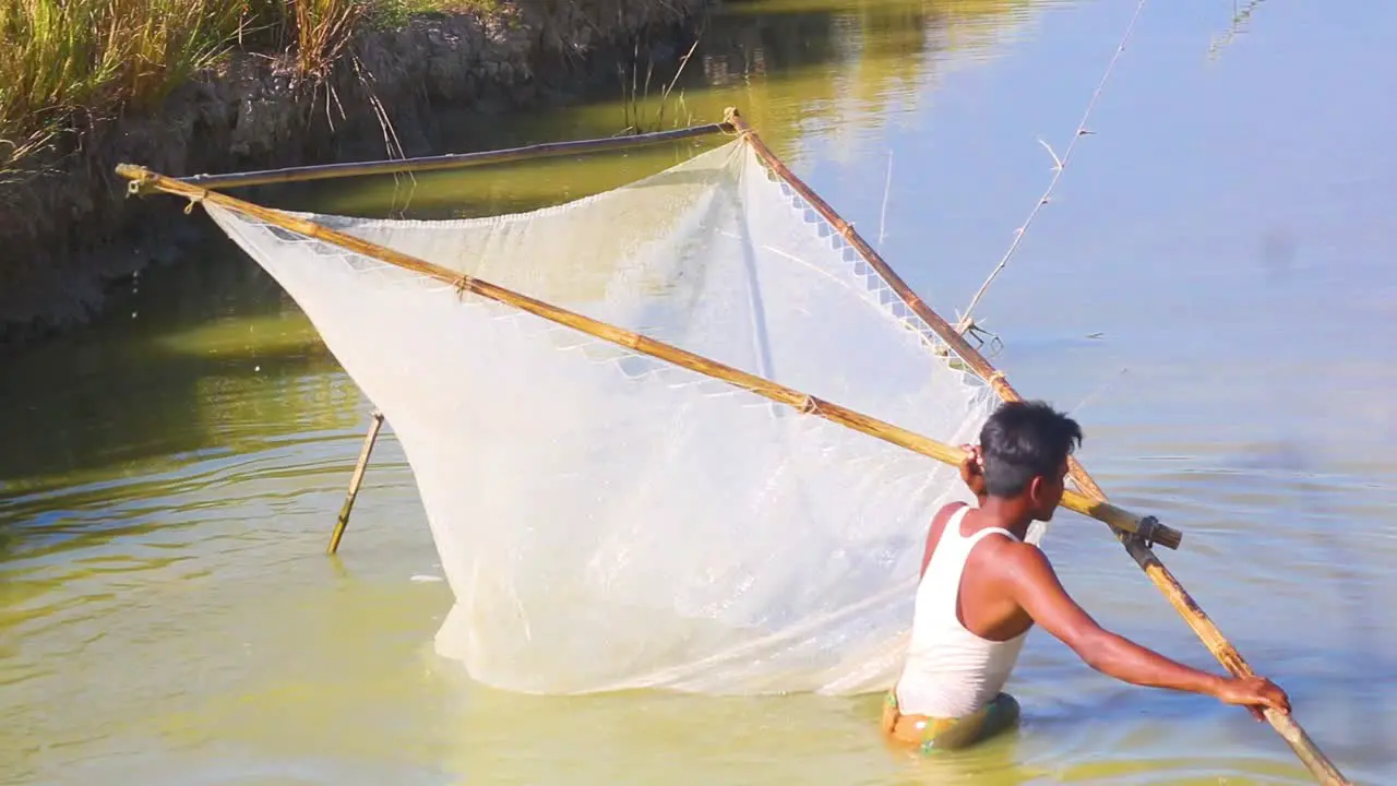 Young fisherman catching fish by traditional fishing net in river of Bangladesh