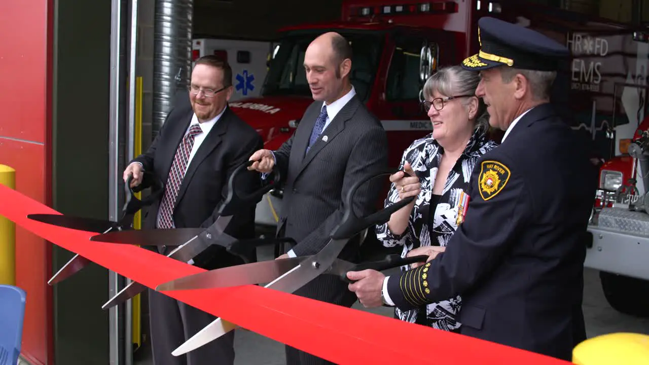 Dignitaries at ribbon cutting ceremonies at a fire hall with big scissors