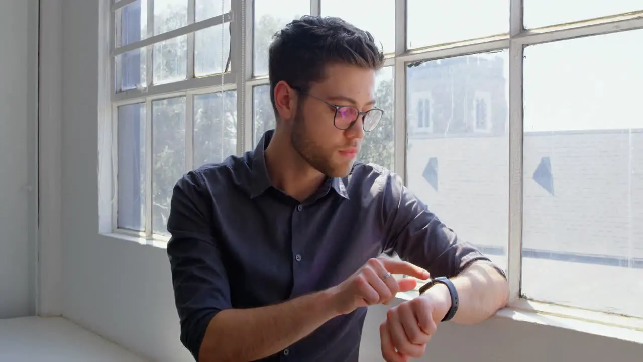 Front view of young caucasian businessman using smartwatch in a modern office 4k