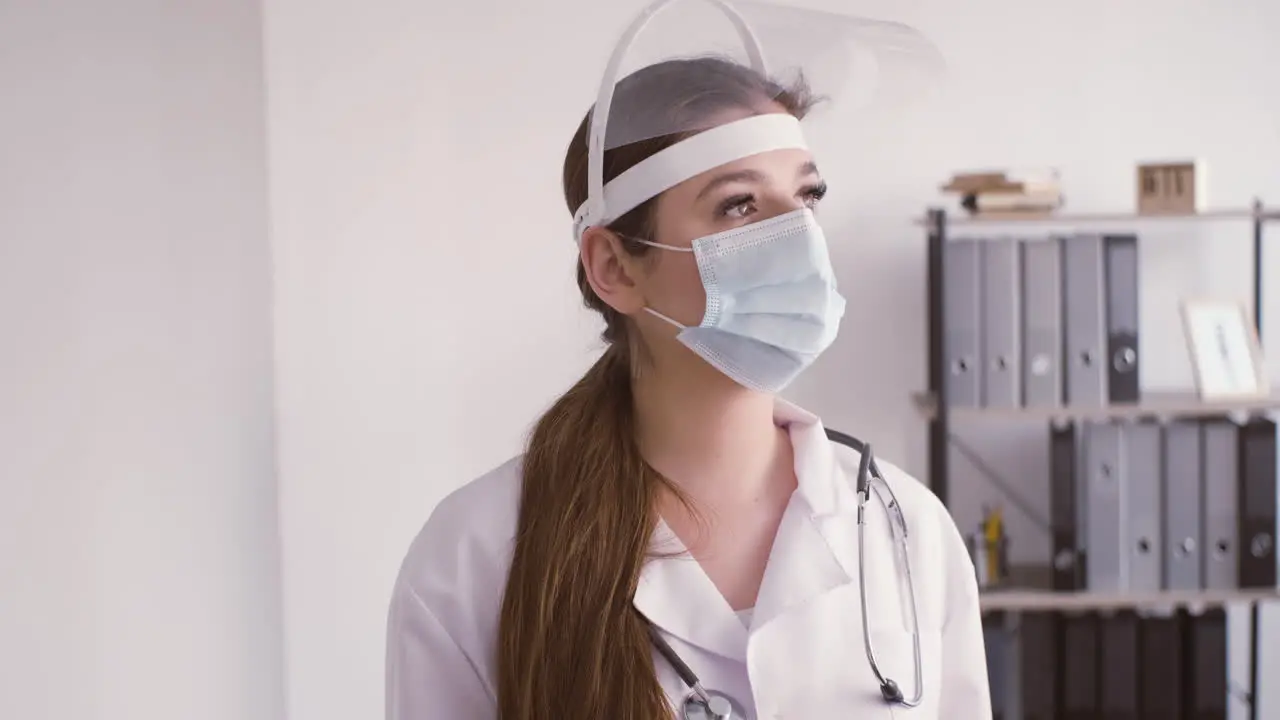 Redhead doctor woman in white coat wearing medical mask and facial screen protection