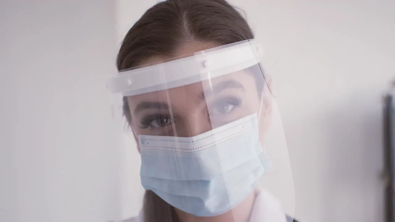 Redhead doctor woman in white coat wearing medical mask and facial screen protection looking at the camera