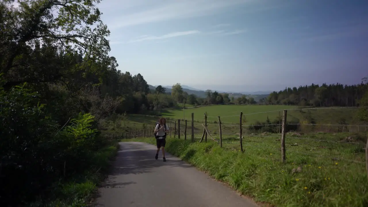 Hiking man tightens backpack strap walking by field forest countryside