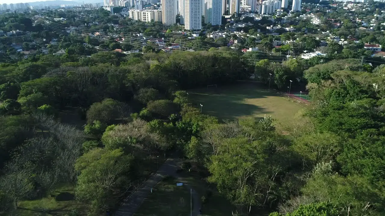 Drone flying in public park with lots of nature and beautiful trees towards soccer field sports health leisure in 4K resolution