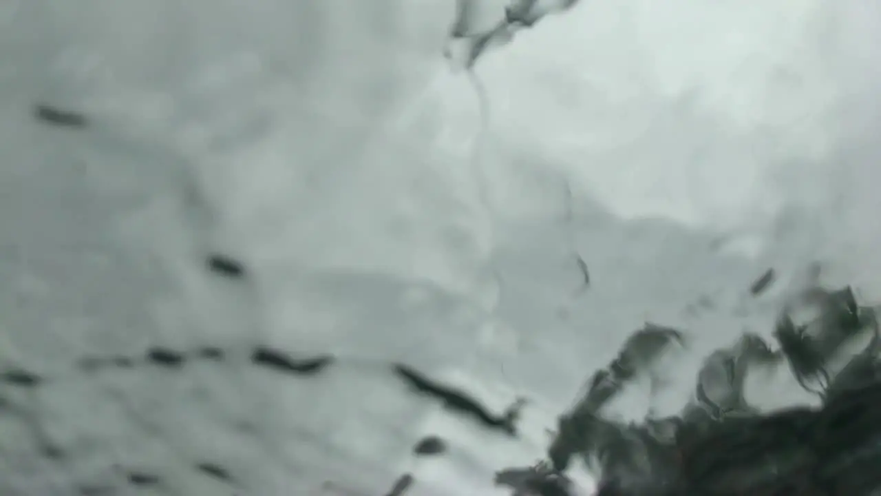 Slow motion abstract view of rain drops landing on glass as seen from below underneath gray sky