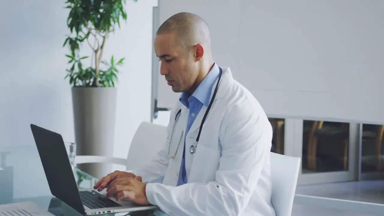 Male doctor using laptop at desk in office 4k