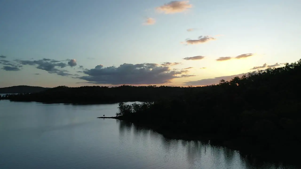 Ascending drone shot flying over Wivenhoe Dam Lake Camera Facing Sun at sunset