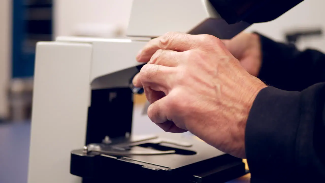 A college professor setting up a slide of cells under a microscope to show his students in a biology laboratory