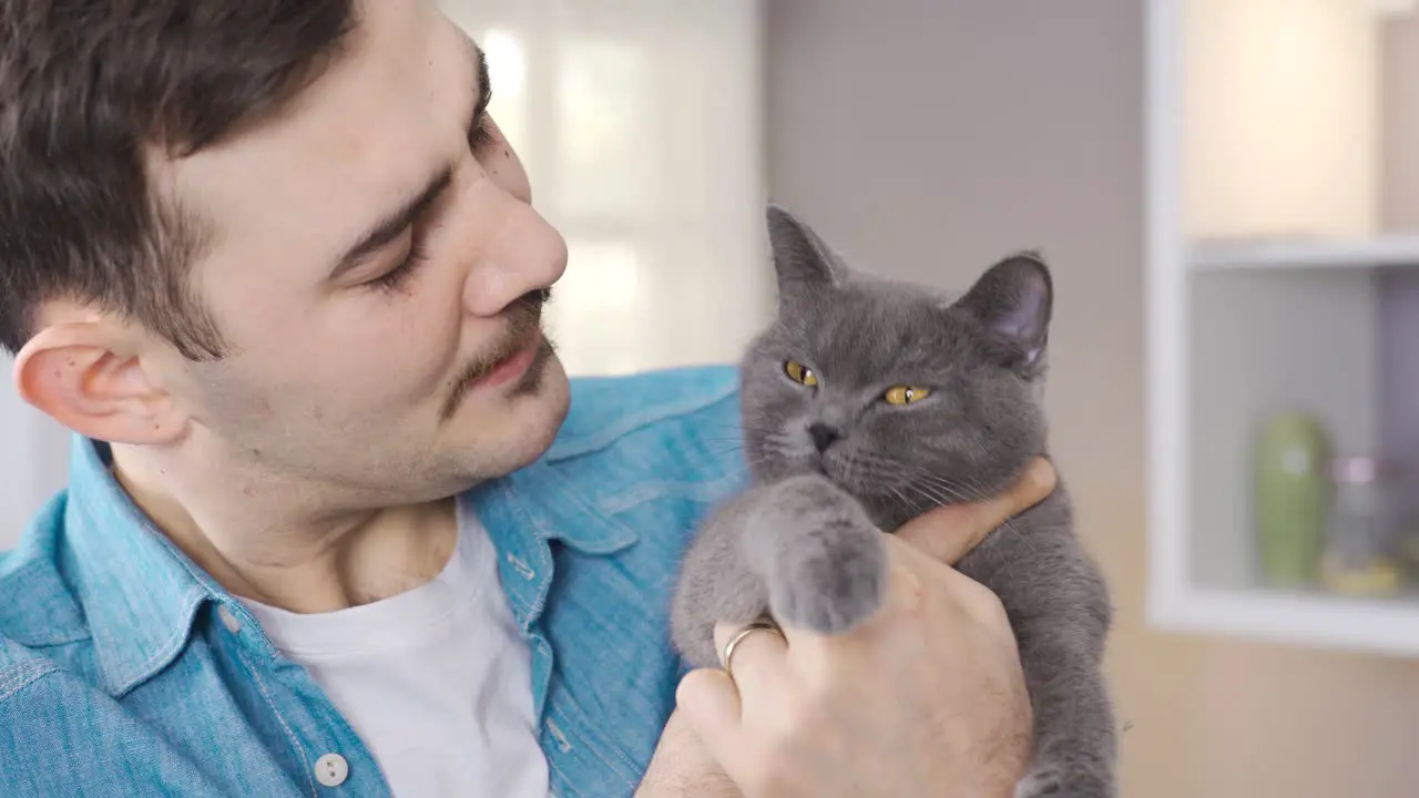 The man holds his gray cat in his lap and looks at him affectionately