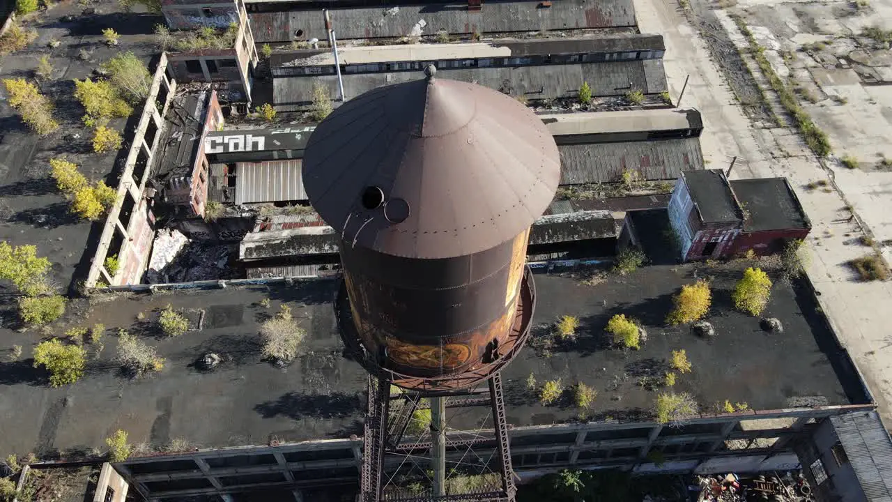 Rusty water tower with open rooftop hatch in abandoned building complex aerial ascend view