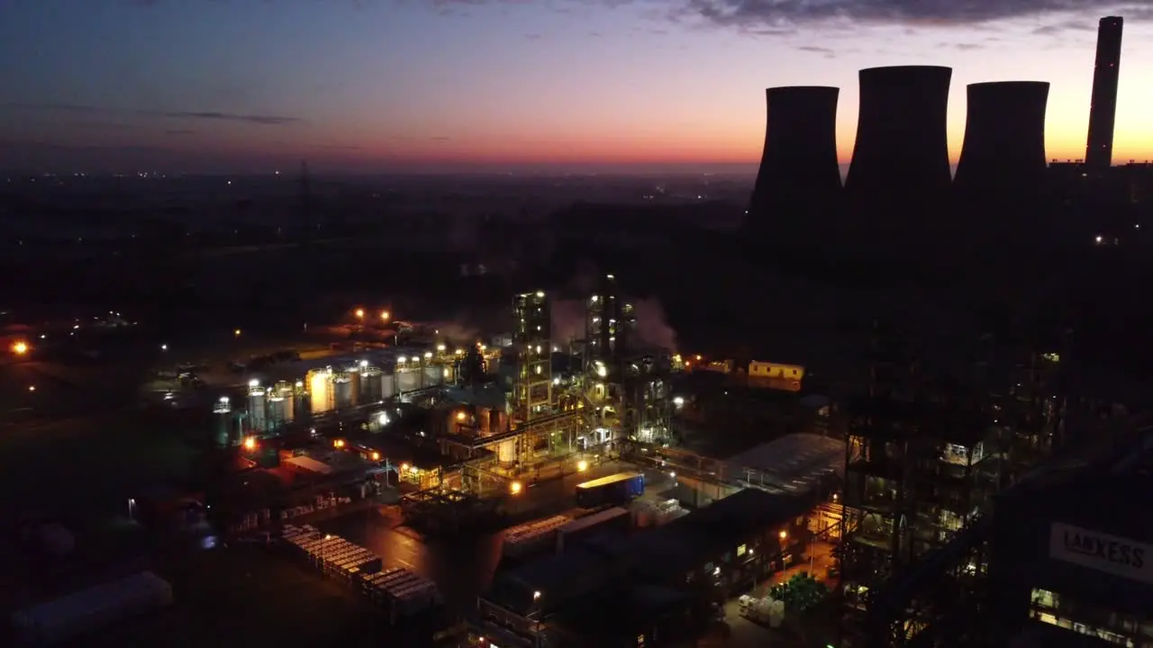 Illuminated aerial night view above industrial pipeline chemical factory site pull away right