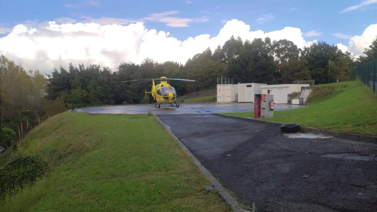 Rescue helicopter at helipad base with maintenance buildings behind a day of white clouds shot traveling left Santiago de Compostela Galicia Spain